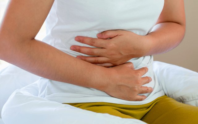 Person holding the abdomen due to belly button discomfort, a common symptom before seeking umbilical hernia diagnosis and treatment.